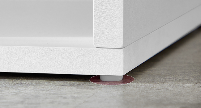 Gros plan du pied du meuble avec de petits coussinets circulaires rouges fixés au bas, conçus pour protéger le sol