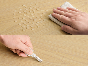 Démonstration de l'application d'un enduit à bois sur une surface en bois clair. Une main applique le produit de remplissage à l'aide d'un couteau à mastic, tandis que l'autre essuie l'excédent avec un chiffon, laissant apparaître plusieurs trous remplis