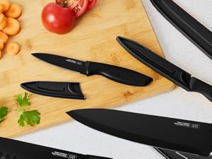 Ensemble de couteaux de cuisine noirs sur planche à découper en bois avec tomates, carottes et persil. Les couteaux comprennent un couteau de chef, un couteau à pain et un couteau d'office avec housses de protection