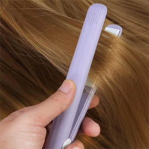 Tenez à la main un peigne en plastique violet muni d'une buse longue et fine, utilisé pour appliquer le produit sur les mèches de cheveux blonds.