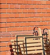 Gros plan d'un mur de briques oranges avec le bord d'un banc ou d'une chaise à lattes de bois visible dans le coin inférieur droit