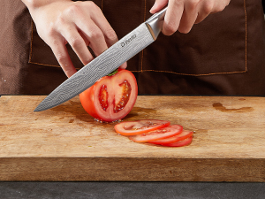tranchant une tomate mûre sur une planche à découper en bois, démontrant ainsi la netteté et la précision du couteau dans