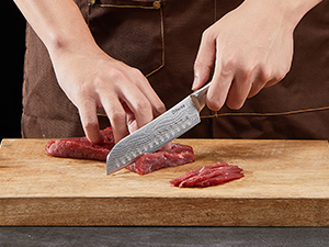 Un couteau tranchant de la viande crue sur une planche à découper en bois, démontrant ainsi une technique de découpe précise