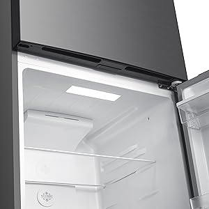 Vue intérieure d'un compartiment de réfrigérateur présentant des étagères en plastique blanc et des rangements dans les portes, illuminés par un éclairage intégré