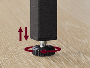 Gros plan d'un pied de meuble ajustable sur un plancher en bois. Le pied noir a une base circulaire rouge avec des bords en forme d'engrenage, permettant un réglage en hauteur