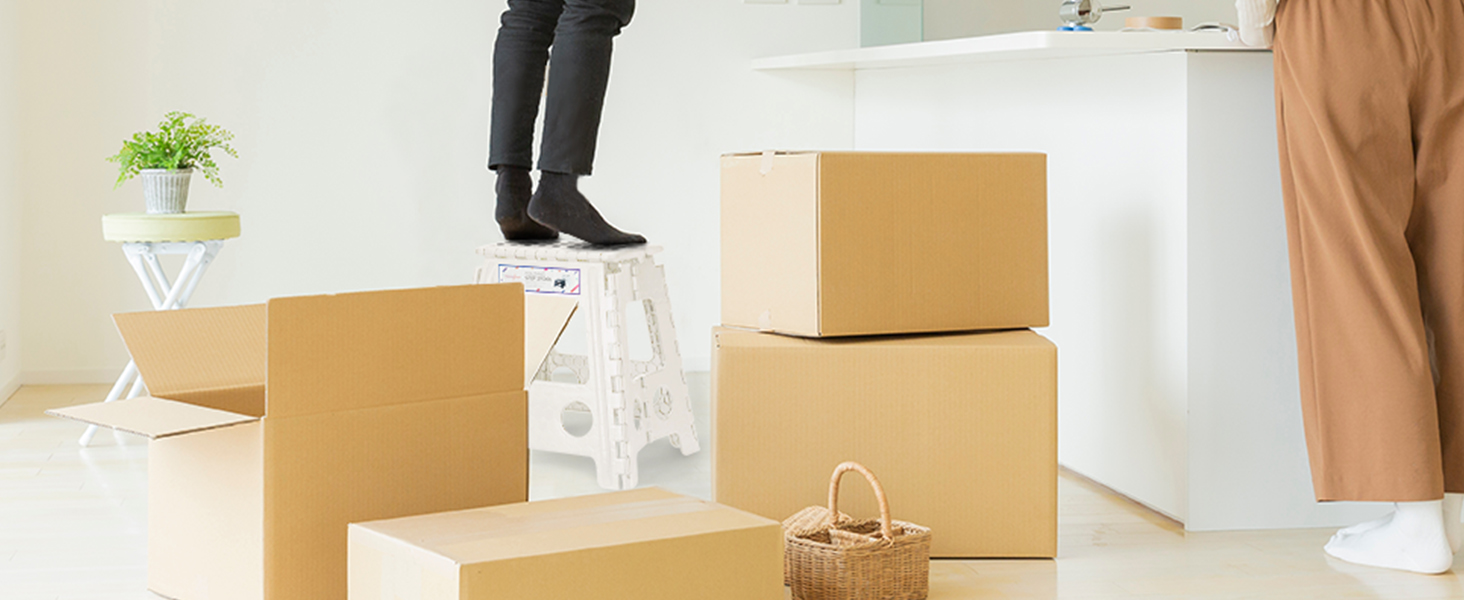 Plusieurs boîtes de déménagement en carton brun empilées sur un sol de couleur claire, avec des jambes de personnes visibles en arrière-plan
