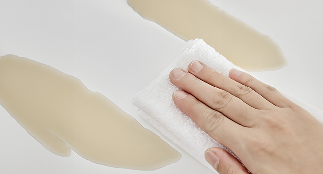 Essuyer à la main une surface blanche avec un chiffon, révélant des traits de peinture beige en dessous. Démonstration d'une technique de nettoyage de peinture ou de surface.