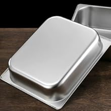 Deux moules à pâtisserie ou récipients alimentaires carrés en acier inoxydable aux bords lisses et arrondis. Un plateau est niché dans l'autre sur une surface sombre.