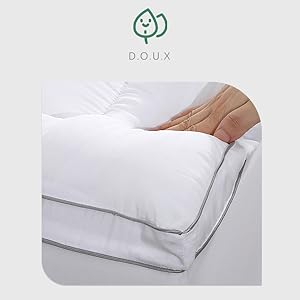 Literie blanche avec la main d'une personne en train de lisser une couette ou une couette en peluche. Logo « DOUX » avec une icône en forme de feuille visible dans le coin supérieur gauche.