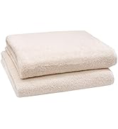 Deux serviettes de bain pliées de couleur crème empilées les unes sur les autres. Les serviettes semblent moelleuses et épaisses avec une surface douce et texturée