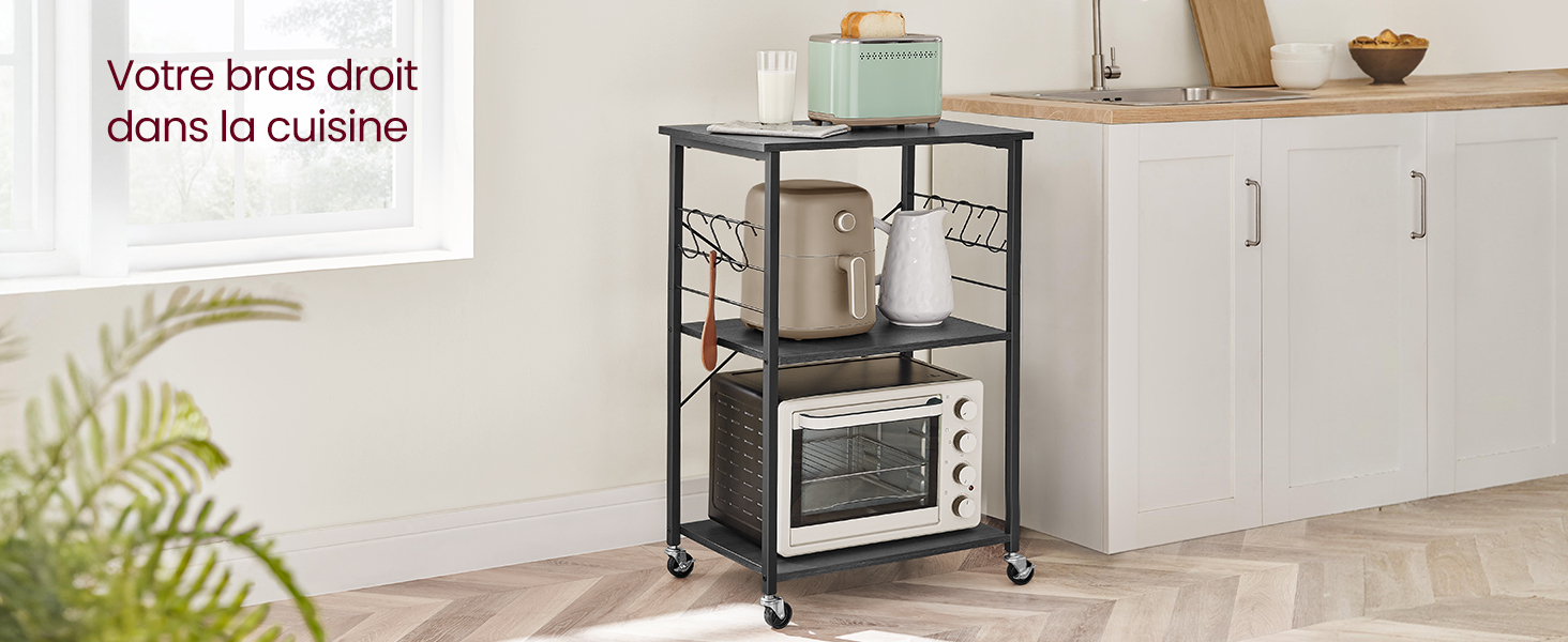 avec four à micro-ondes sur l'étagère supérieure. Structure en métal noir, étagères en bois et roulettes pour faciliter la mobilité. Armoires blanches en arrière-plan.