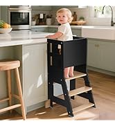 Tour d'apprentissage/tabouret d'aide de cuisine en bois noir avec rails de sécurité positionnés contre un comptoir de cuisine blanc. Dispose de plusieurs plates-formes de hauteur pour se tenir debout.