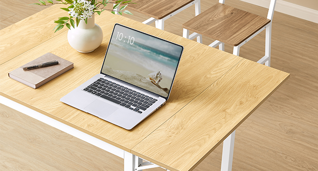 sur une surface de bureau en bois clair, avec un vase blanc contenant des plantes vertes et un carnet à côté.