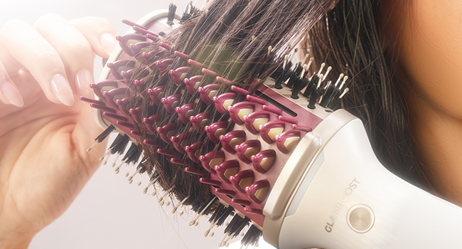 Vue rapprochée du processus de coiffure montrant des cheveux sectionnés avec un outil de coiffage rose utilisé.