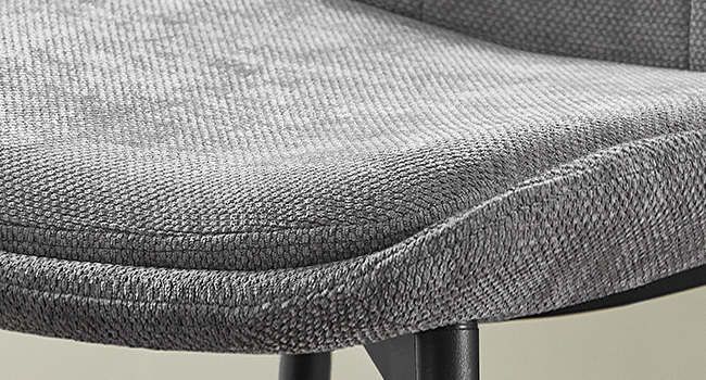 Gros plan d'un coussin de chaise avec revêtement en tissu texturé gris. Le coussin a un bord incurvé et semble être attaché à un cadre en métal noir.