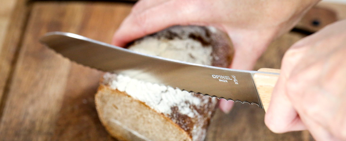 Gros plan des mains à l'aide d'un grand couteau de cuisine pour trancher une miche de pain dont la garniture ou la pâte à tartiner est blanche