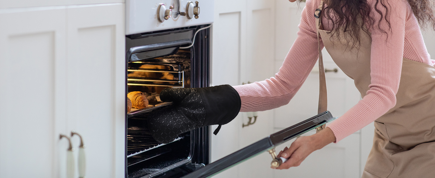 Personne portant un chandail rose et un gant de cuisine, ouvrant la porte d'un four de cuisine avec des produits de boulangerie visibles à l'intérieur sur une grille