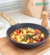 Poêle antiadhésive contenant des légumes cuits colorés, photographiée d'en haut avec des accessoires de cuisine en bois visibles en arrière-plan