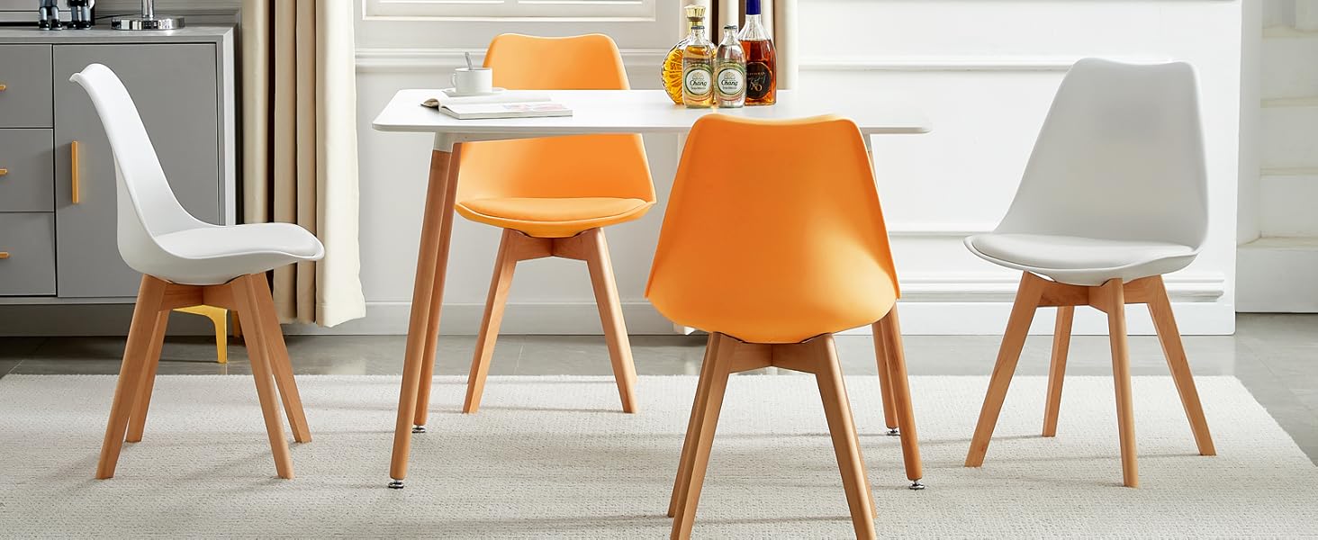 avec table ronde blanche et quatre chaises. Deux chaises oranges et deux chaises blanches avec pieds en bois. Art abstrait sur mur.