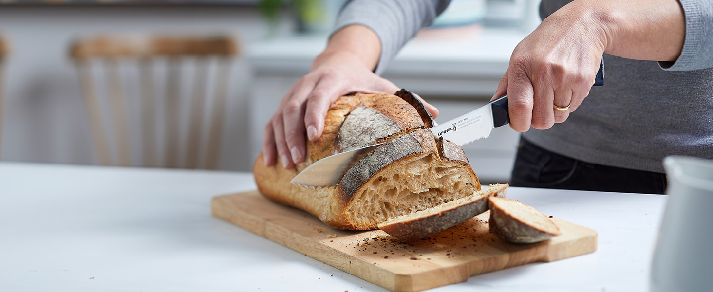 Personne tranchant une miche de pain artisanal sur une planche à découper en bois, à l'aide d'un couteau dentelé