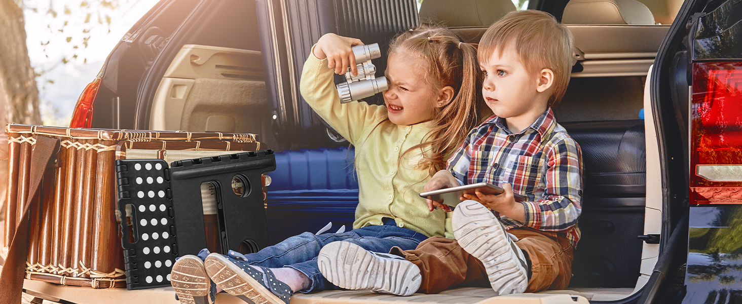 Deux enfants assis dans la zone de chargement ouverte d'un véhicule, entourés de conteneurs de rangement et de matériel de voyage.