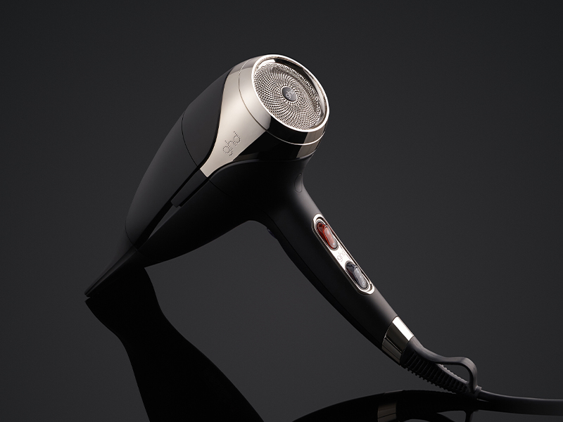 Sèche-cheveux noir professionnel avec attache argentée photographié sur fond sombre avec reflet en dessous.
