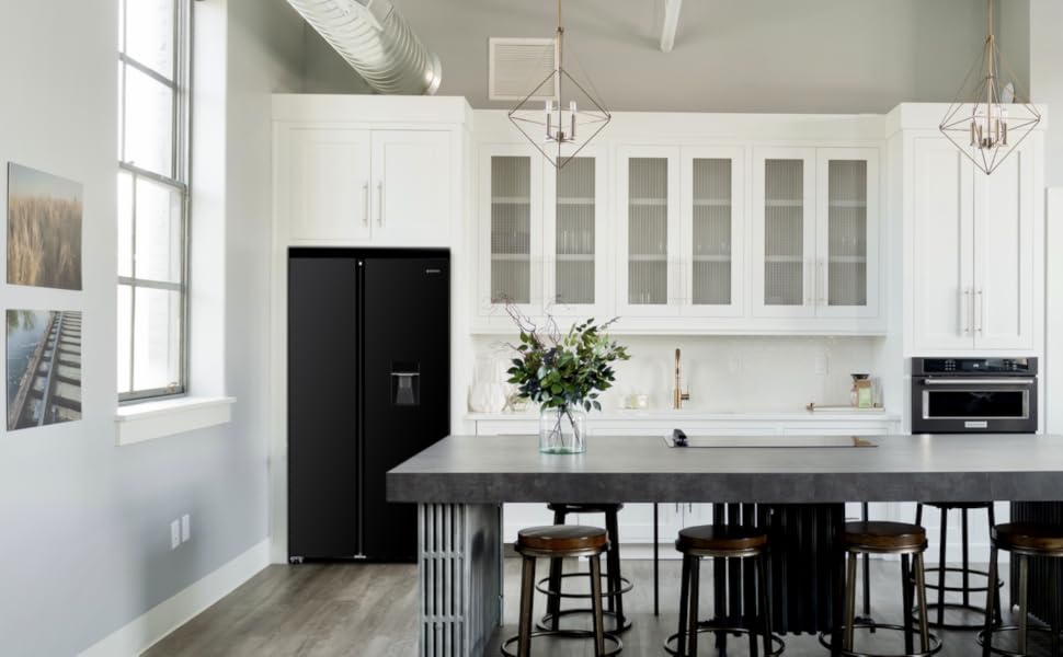 Cuisine blanche moderne avec grand îlot, réfrigérateur noir, lampes suspendues et planchers de bois franc. Les armoires ont des façades vitrées.