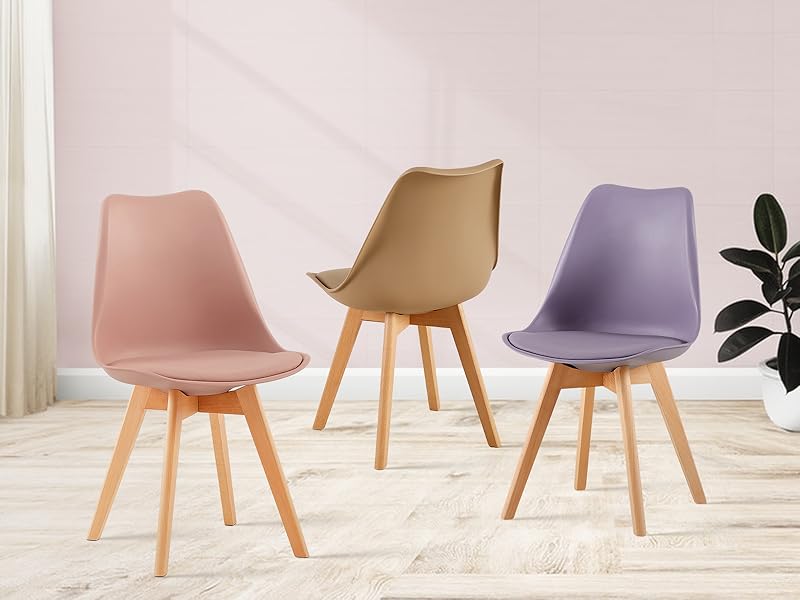 Trois chaises de salle à manger modernes aux couleurs pastel (rose, beige et violet) avec pieds en bois, adossées à un mur de couleur claire et à un plancher en bois
