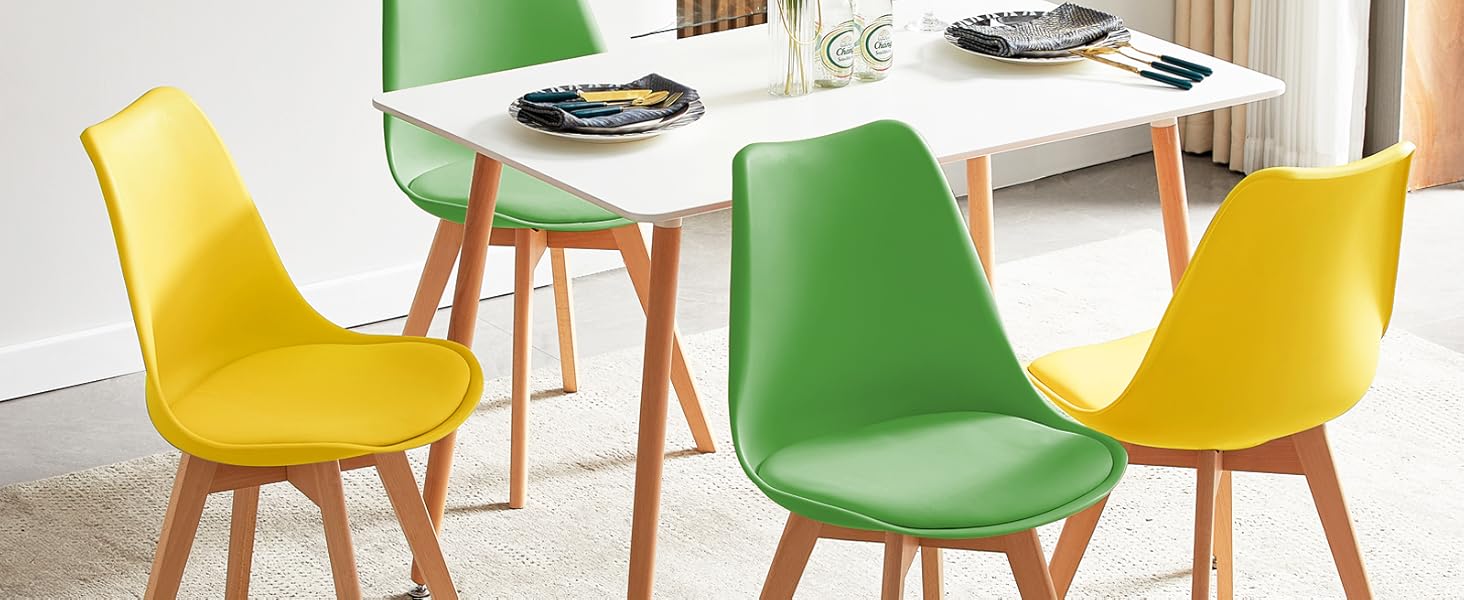avec table rectangulaire blanche et quatre chaises, deux vertes et deux jaunes. Pieds de chaise en bois et couverts visibles sur la table.