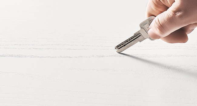 Tenez à la main une clé de porte en métal avec une poignée en plastique, posée sur une surface blanche. La lame de la clé présente des encoches et des rainures distinctes