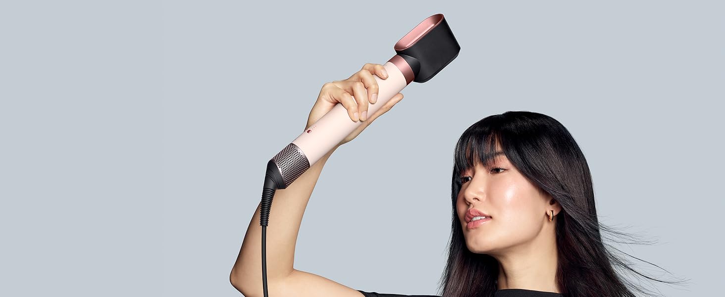 Profil latéral d'une personne utilisant un outil de coiffage portable avec des cheveux noirs fluides sur fond gris.