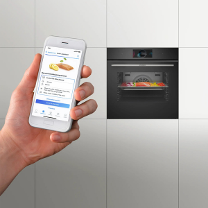 Image fractionnée montrant la main tenant un smartphone avec l'interface de l'application à gauche et un four encastré noir ou un écran d'appareil à droite.