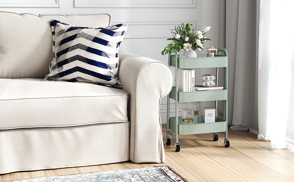 Coin salon avec canapé beige, coussin rayé bleu-blanc et chariot roulant vert menthe. Le chariot contient des livres, des décorations et des arrangements floraux. Plancher de bois franc avec tapis à motifs visibles