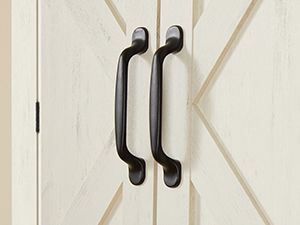 Gros plan de deux poignées de porte en métal noir montées sur une porte de style grange en bois blanc. Les poignées sont longues, incurvées et ont une finition mate.