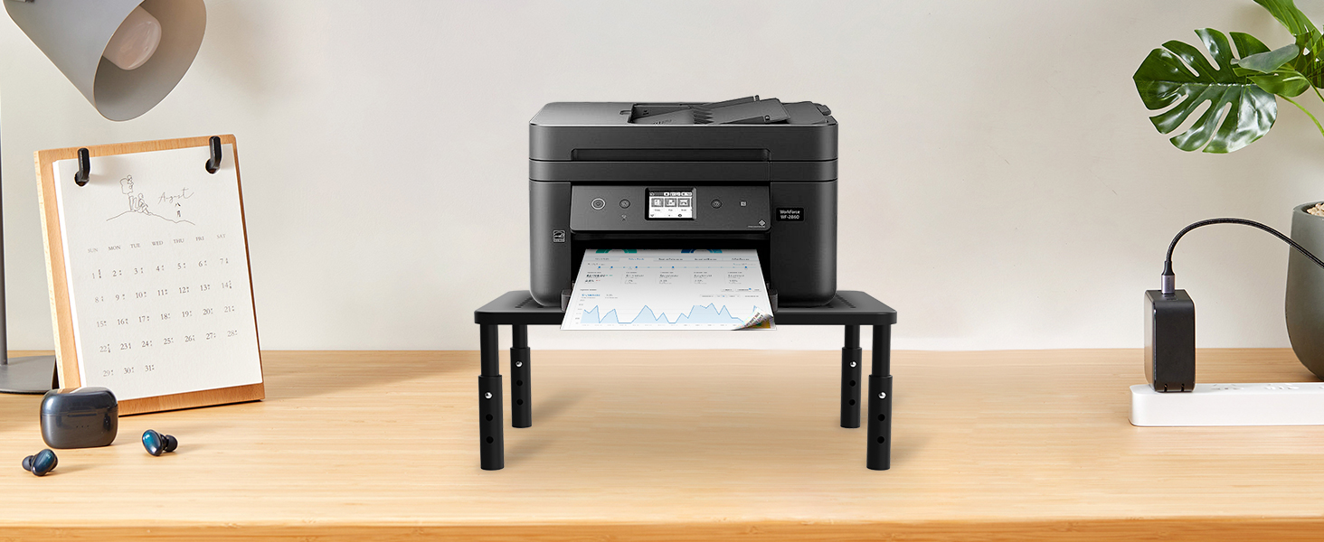 Support d'imprimante noir sur bureau en bois avec design de support d'écran, avec des accessoires d'organisation du bureau et une plante en arrière-plan.