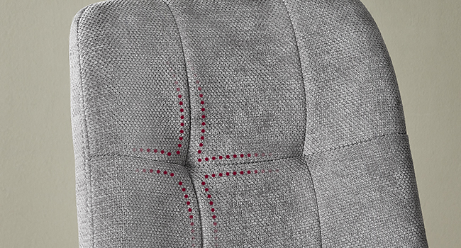 Détail de meuble rembourré gris montrant un motif de coutures capitonnées en fil bordeaux formant un motif en croix ou