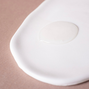 Gros plan d'une substance blanche et crémeuse sur une surface lisse. La texture semble soyeuse et s'étale en forme de cercle sur un fond rose clair.