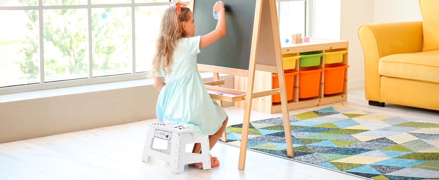 Aménagement de salle de jeux pour enfants avec chevalet en bois, bacs de rangement colorés, fauteuil jaune et tapis à motifs
