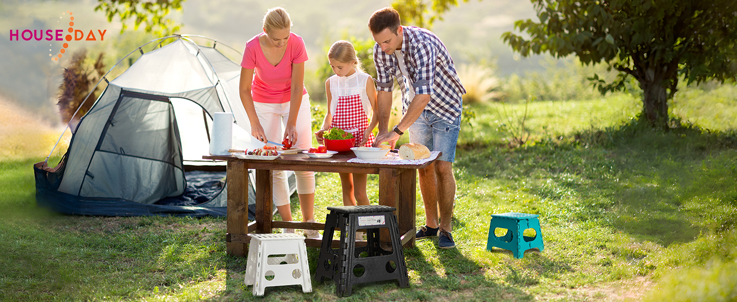 Scène de camping en plein air avec une famille préparant à manger à une table près d'une tente bleue. Tabourets pliants et gazon vert visibles.