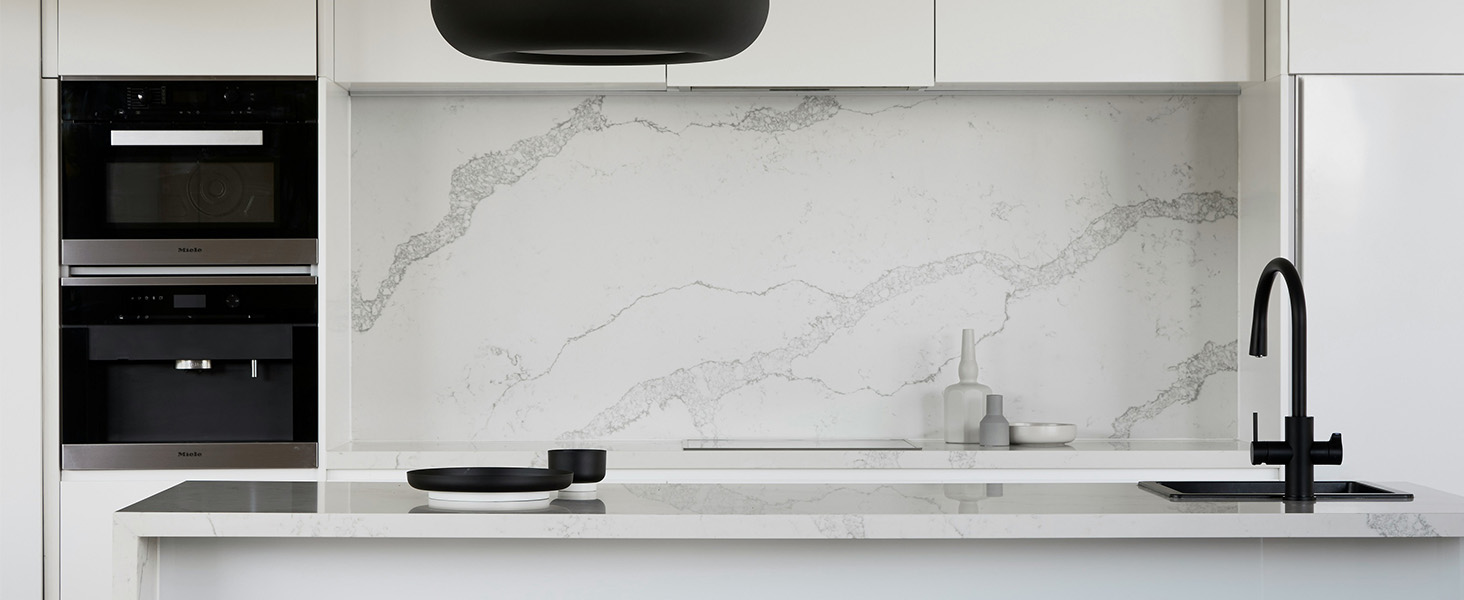 Intérieur de cuisine minimaliste moderne avec dosseret en marbre blanc, luminaires noirs, appareils électroménagers intégrés et plans de travail élégants avec évier intégré