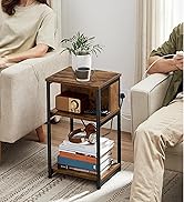 Table d'appoint à trois niveaux avec étagères en bois et structure en métal, contenant des plantes, des tasses, des livres et des objets de décoration. Placé entre deux canapés dans un décor de salon.