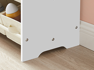 Vue rapprochée d'une base ou d'un panneau de meuble blanc avec des vis de montage visibles, positionné contre un plancher et une plinthe en bois clair