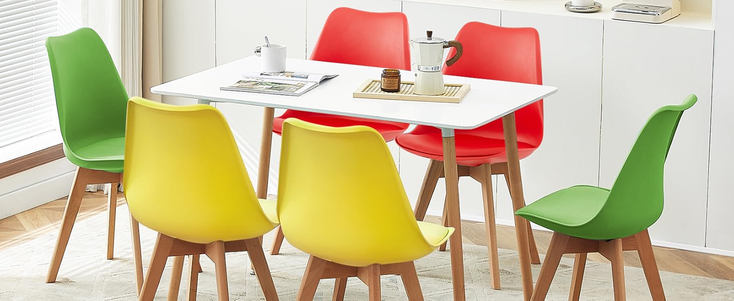 avec table blanche et chaises colorées en rouge, jaune et vert. Meuble de rangement blanc et décor en arrière-plan.