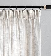 avec embout doré, supportant des rideaux en lin blanc transparent. La tringle comporte plusieurs anneaux de suspension et est montée contre un mur gris clair.