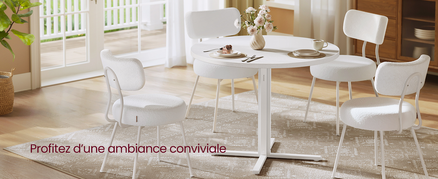 avec quatre chaises blanches assorties, située dans une pièce lumineuse avec fenêtres. La table est dressée avec des assiettes et des tasses pour un repas.