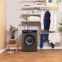 Intérieur de la buanderie moderne avec machine à laver, étagère avec vêtements pliés et vêtements suspendus dans un espace organisé.