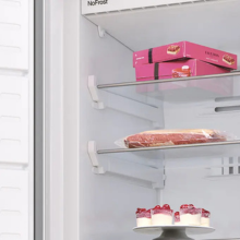 Vue de l'étagère intérieure du réfrigérateur montrant des contenants ou des plateaux de rangement roses disposés sur des étagères en verre transparent.