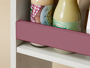 Vue partielle d'une étagère blanche contenant des bouteilles en verre avec des étiquettes colorées. Une cloison en bois peinte en rose est visible au premier plan