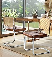 Deux chaises de salle à manger à dossier en canne avec des sièges en cuir brun et des cadres en porte-à-faux chromés, positionnées sur une table en bois près de grandes