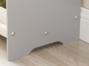 Gros plan d'une base de meuble grise ou d'une pièce de support avec des vis de montage visibles, positionnée contre un sol de couleur claire